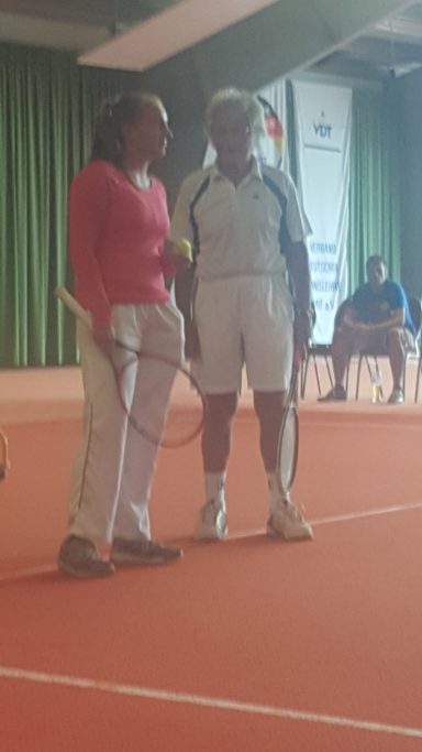 Zwei Tennis-Spieler in Sportkleidung stehen auf einem Tennisplatz und sprechen.